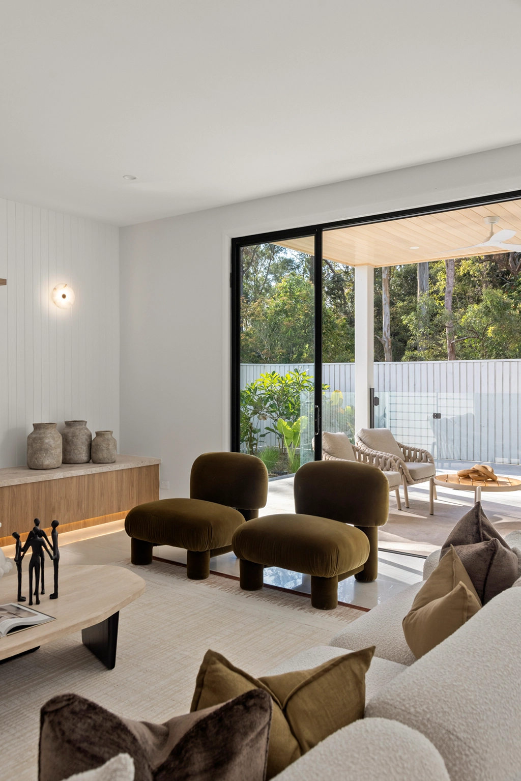 Canopy living room with sculptural olive chairs, natural finishes and seamless connection to the outdoor living area.